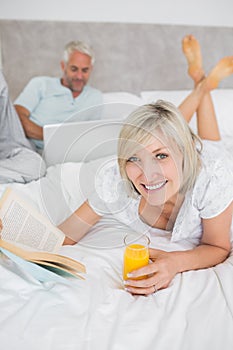 Couple reading book and using laptop in bed