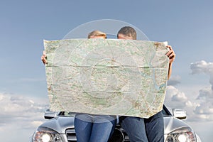 Couple reading map while leaning on car hood during road trip photo