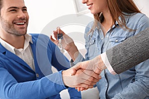 Couple at real estate sales office with agent shaking hands deal
