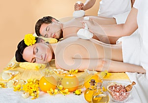 Couple Receiving Massage With Herbal Compress Stamps At Spa