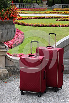 Couple of red suitcases in front of ornamental flowerbeds. Mirabell palace gardens. Park in Salzburg town in Austria