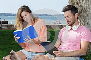 couple relax on deckchair reading book and tablet outdoors