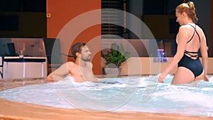 Couple relaxes in an outdoor hot tub. Happy young woman and man relaxing in hot water near the pool.