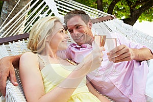 Couple Relaxing In Beach Hammock Drinking Champagne