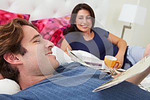 Couple Relaxing In Bed With Coffee And Newspaper