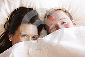 Couple Relaxing In Bed Hiding Under Bedclothes photo