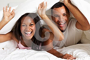 Couple Relaxing In Bed Hiding Under Duvet