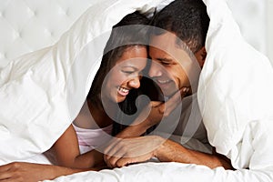 Couple Relaxing In Bed Hiding Under Duvet