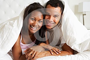 Couple Relaxing In Bed Hiding Under Duvet