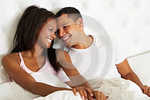 Couple Relaxing In Bed Wearing Pajamas