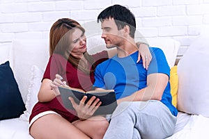 Couple relaxing with book reading in the living room on white sofa couch. Close-up of romantic couple laughing together