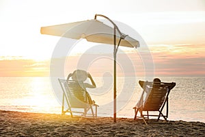 Couple relaxing on deck chairs at beach. Summer vacation