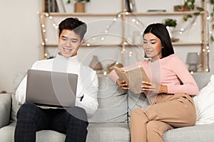 Couple Relaxing Enjoying Weekend Reading Book And Using Laptop Indoor
