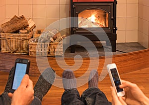 Couple relaxing by fire looking at separate mobile devices