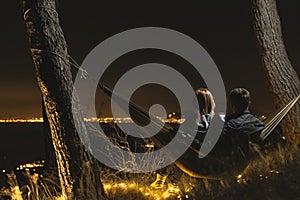 Couple relaxing in a hammock and enjoying starry sky. View from the top of the mountain to the lights of the city of Naples.