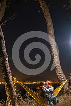 Couple relaxing in a hammock and kissing. View from the top of the mountain to the lights of the city of Naples. Volcano Vesuvio.