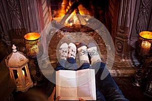 Couple relaxing at home reading a book. Feet in wool socks near fireplace. Winter holiday concept