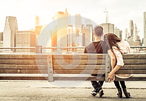 Couple relaxing on New york bench in front of the skyline at sun