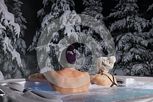 Couple relaxing in outdoor hot tub and enjoying snowy winter forest landscape at spa resort