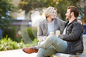 Couple Relaxing On Park Bench With Takeaway Coffee