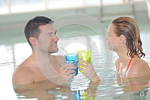 Couple relaxing in resort swimming pool drinking cocktails