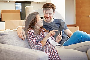 Couple Relaxing On Sofa With Digital Tablet In New Home