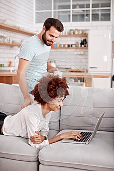 Couple Relaxing On Sofa At Home Looking At Laptop Together