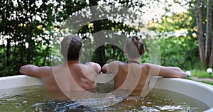 couple relaxing together in outdoor hot tub at forest resort. spa nature treatment, romantic getaway