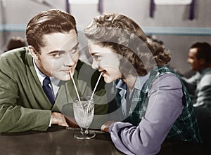 Couple in a restaurant looking at each other and sharing a milk shake with two straws photo