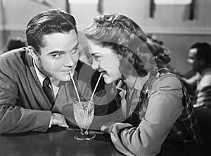 Couple in a restaurant looking at each other and sharing a milk shake with two straws