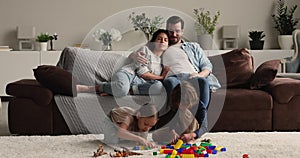 Couple resting on couch looking at children play on floor