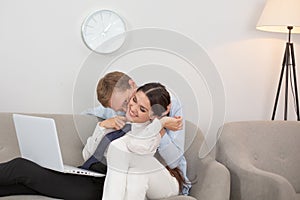 Couple resting on couch using laptop. Married couple having some relaxed time on sofa at home. Man kissing his