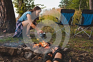 couple resting near bonfire. woman cooking outdoors on fire