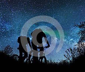 Couple ride bicycles at night under the milky way