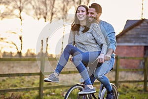 Couple Riding Bike Through Countryside With Woman Sitting On Handlebars