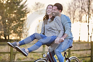 Couple Riding Bike Through Countryside With Woman Sitting On Handlebars