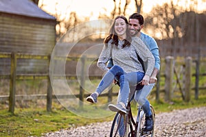 Couple Riding Bike Through Countryside With Woman Sitting On Handlebars