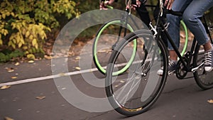 Couple riding bikes along the asphalt road in local park early in the morning in autumn day. Close up of legs pedaling