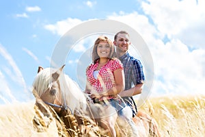 Couple riding on horse in meadow