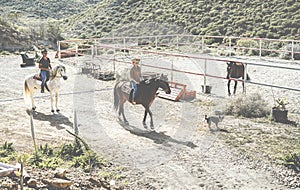 Couple riding horses starting from ranch with their dogs following them - Happy people having fun on summer day - Tour, excursion