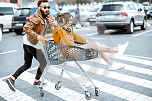 Couple riding with shopping cart on the parking outdoors
