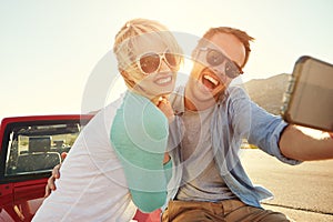 Couple On Road Trip Sit On Convertible Car Taking Selfie