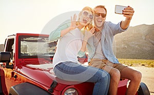 Couple On Road Trip Sit On Convertible Car Taking Selfie photo
