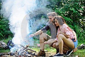 Couple roasting sausages on sticks nature background. Traditional roasted food as attribute of picnic. Camping and