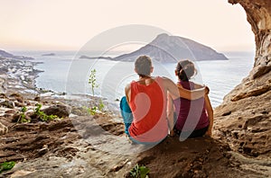 Couple of rock climbers having rest while sitting at bottom of cliff and enjoying picturesque view of Telendos Island in front