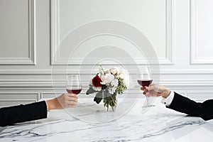 Couple on romantic date. Friends clinking glasses, side view. Red wine, flowers around on marble table. Wedding celebration, party