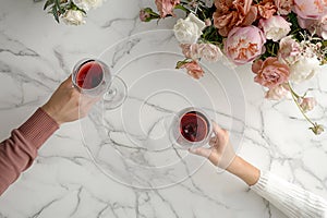 Couple on romantic date. Friends clinking glasses, top view. Red wine, flowers around on marble table. Wedding celebration, party