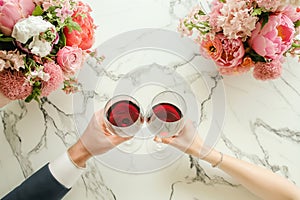 Couple on romantic date. Friends clinking glasses, top view. Red wine, flowers around on marble table. Wedding celebration, party