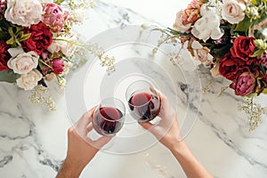 Couple on romantic date. Friends clinking glasses, top view. Red wine, flowers around on wooden table. Wedding celebration, party