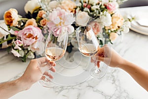 Couple on romantic date. Friends clinking glasses, top view. White wine, flowers around on marble table. Wedding celebration,